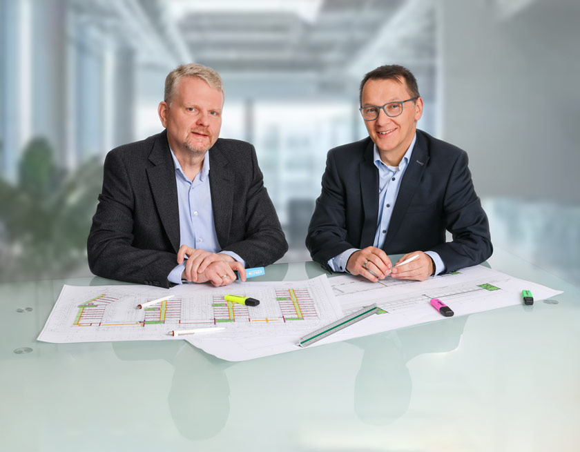 Die INgenieure Heistermann und D&ouml;ring sitzen an einem Schreibtisch mit Glasplatte